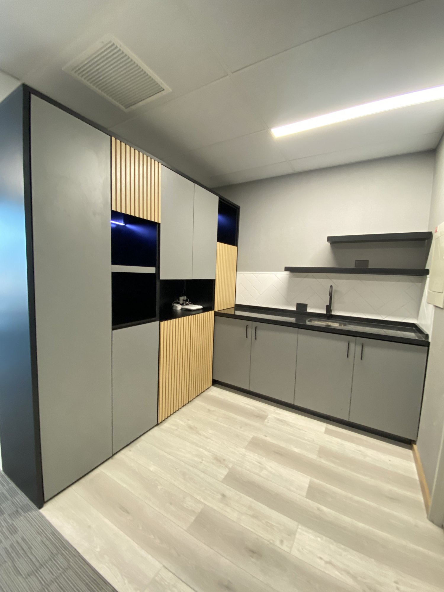 Kitchenette con mobiliario gris, detalles de madera y cubierta oscura
