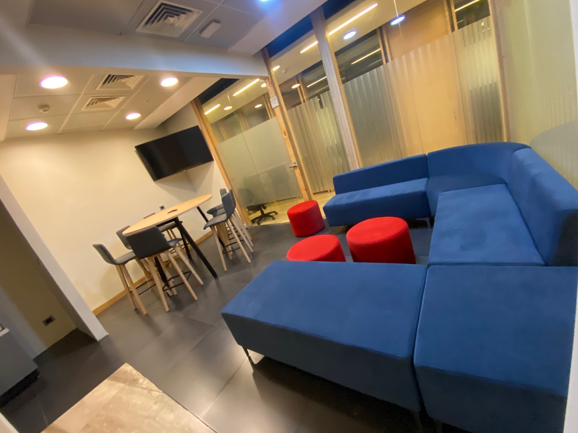 Espacio de encuentro con sofá azul, poufs rojos y mesas altas