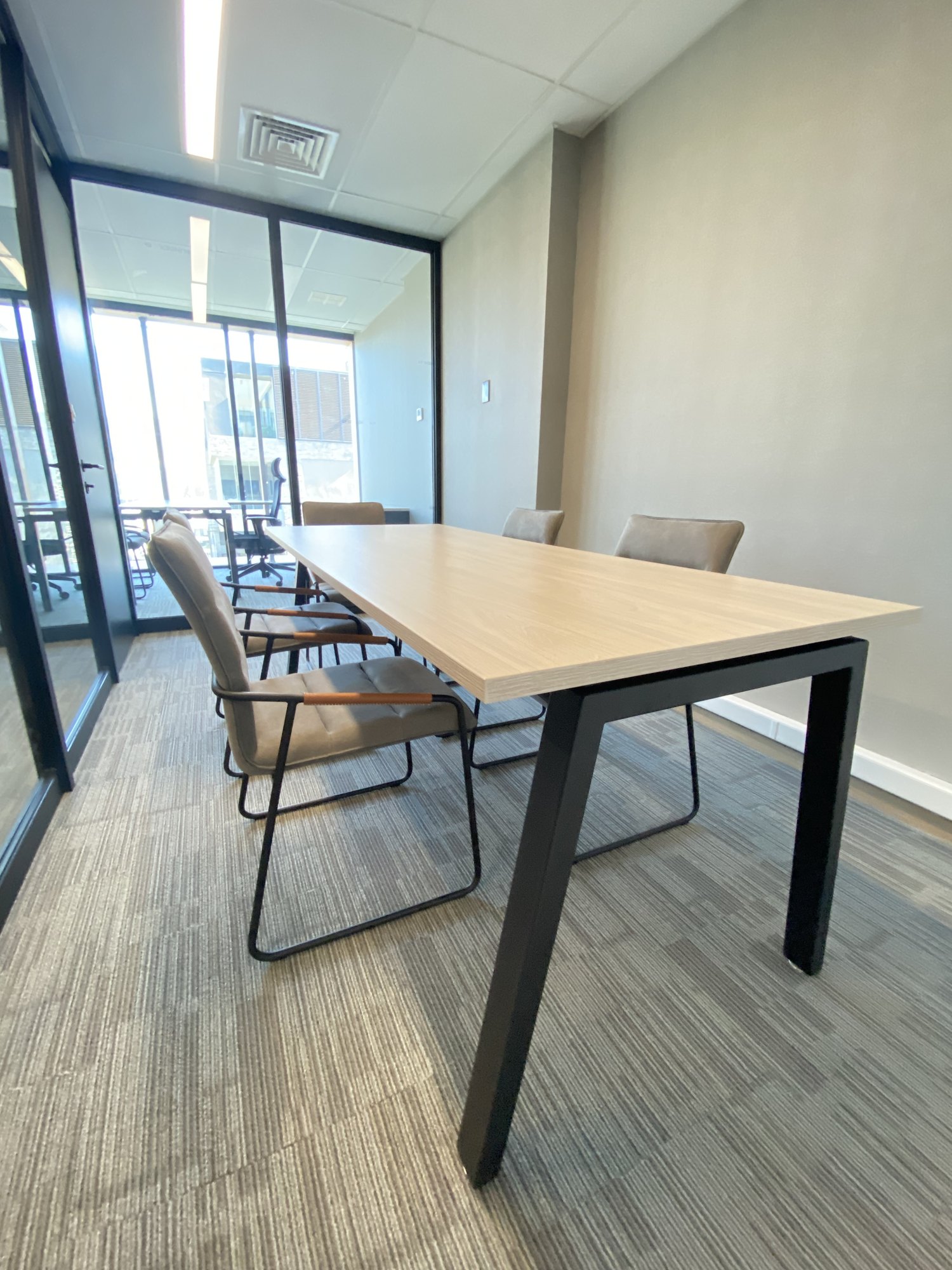 Sala de reunión con mesa clara, sillas tapizadas y piso alfombrado