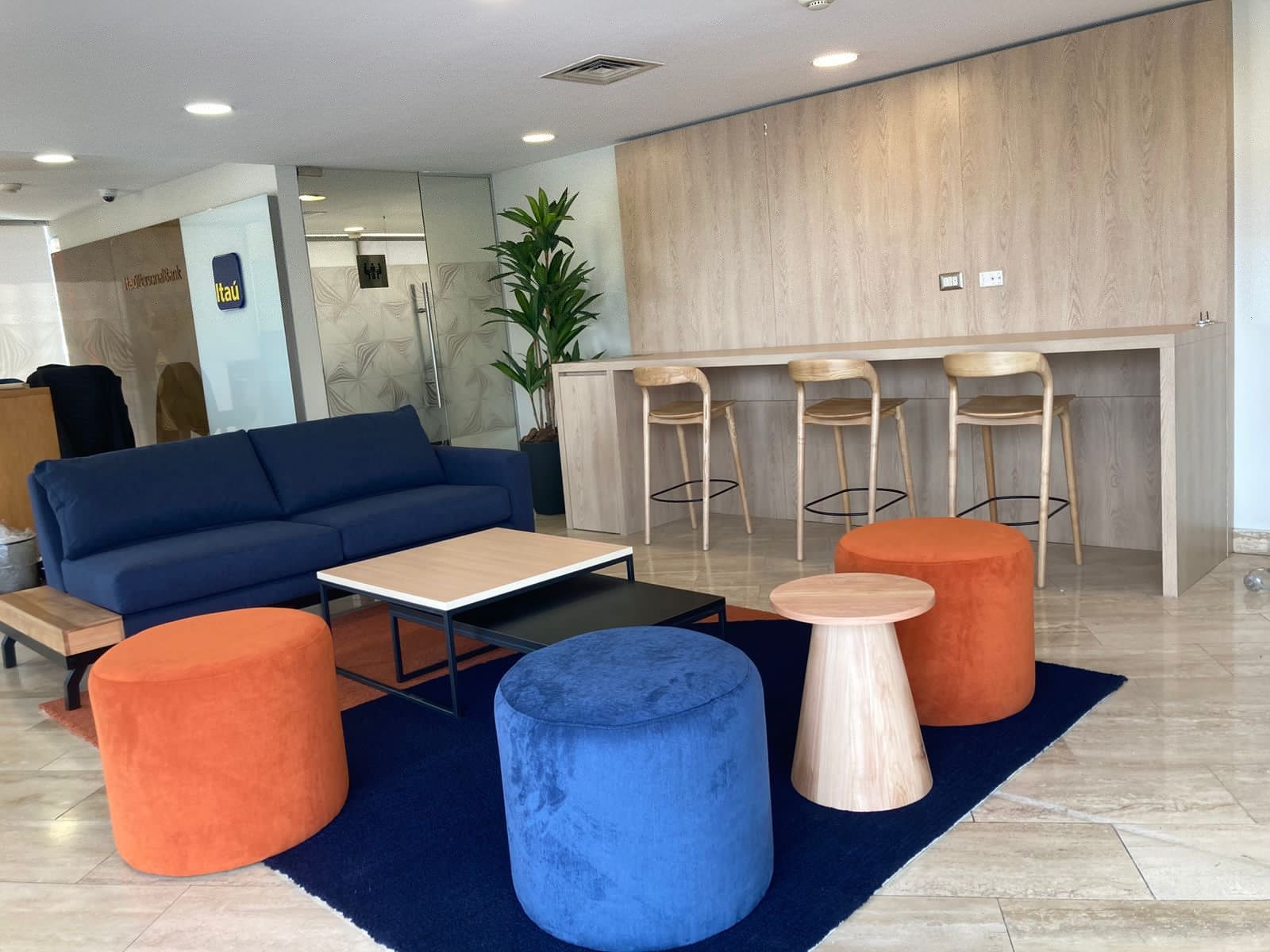 Zona de encuentro con sofá azul, asientos de colores y barra con sillas altas